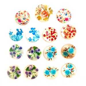 May include: Assortment of 15 round, white, shell-like, decorative embellishments with various floral patterns. The embellishments have a hole in the top for hanging or attaching.