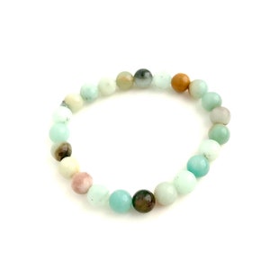 May include: A bracelet made of various green, brown, and pink gemstone beads. The beads are round and have a smooth, polished finish.