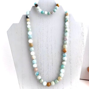 May include: A light blue and brown beaded necklace and bracelet set. The necklace is long and the bracelet is shorter. The beads are round and have a natural, earthy look.