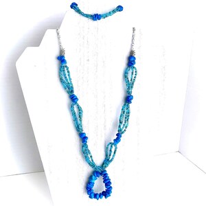 May include: A turquoise blue beaded necklace and bracelet set. The necklace features a teardrop pendant and the bracelet is a simple band.