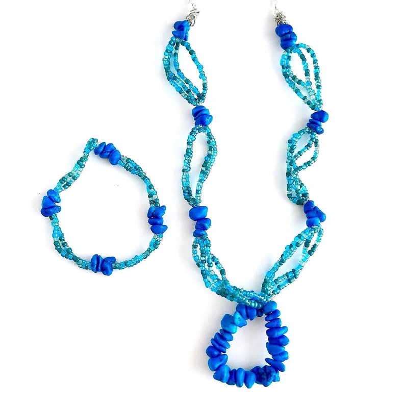 May include: A blue and turquoise beaded necklace and bracelet set. The necklace has a pendant in the shape of a circle.