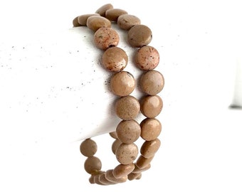 May include: A double-strand bracelet made with light brown, round, flat, natural stone beads.