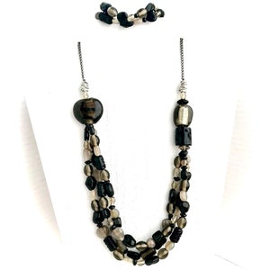 May include: A multi-strand necklace with black, gray, and silver beads. The necklace features a large, heart-shaped bead and a silver and black bead.