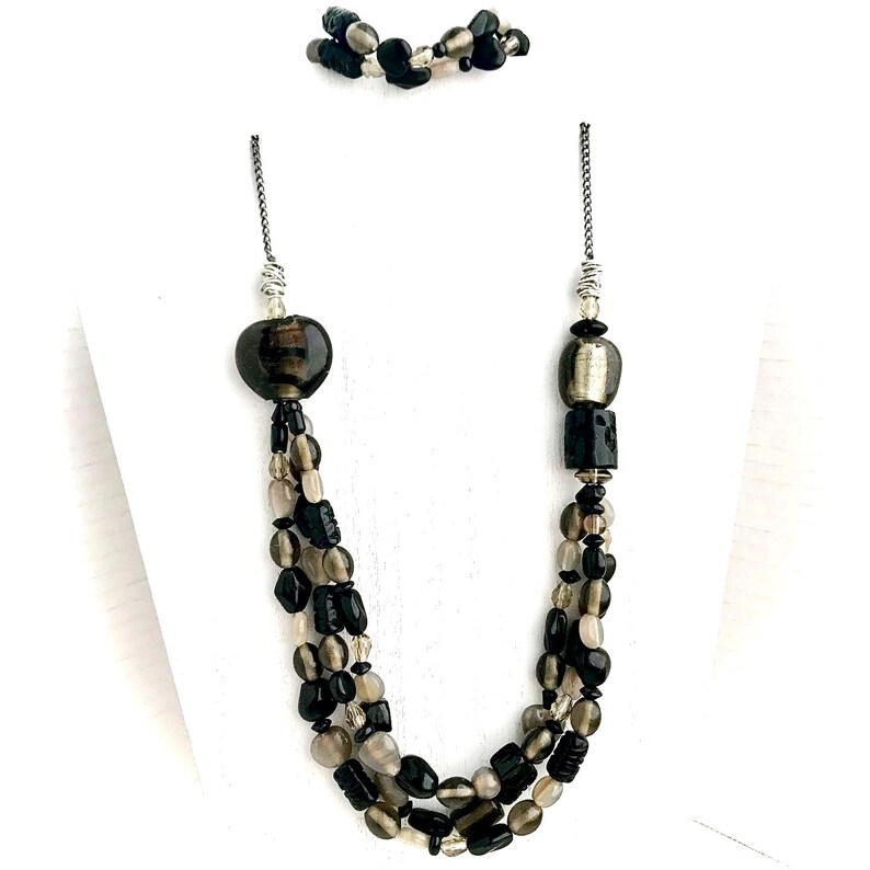 May include: A multi-strand necklace with black, gray, and silver beads. The necklace features a large, heart-shaped bead and a silver and black bead.