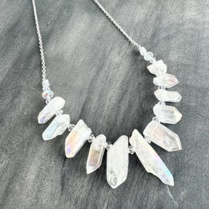 May include: A silver chain necklace with iridescent clear quartz crystal points. The necklace is on a gray background.