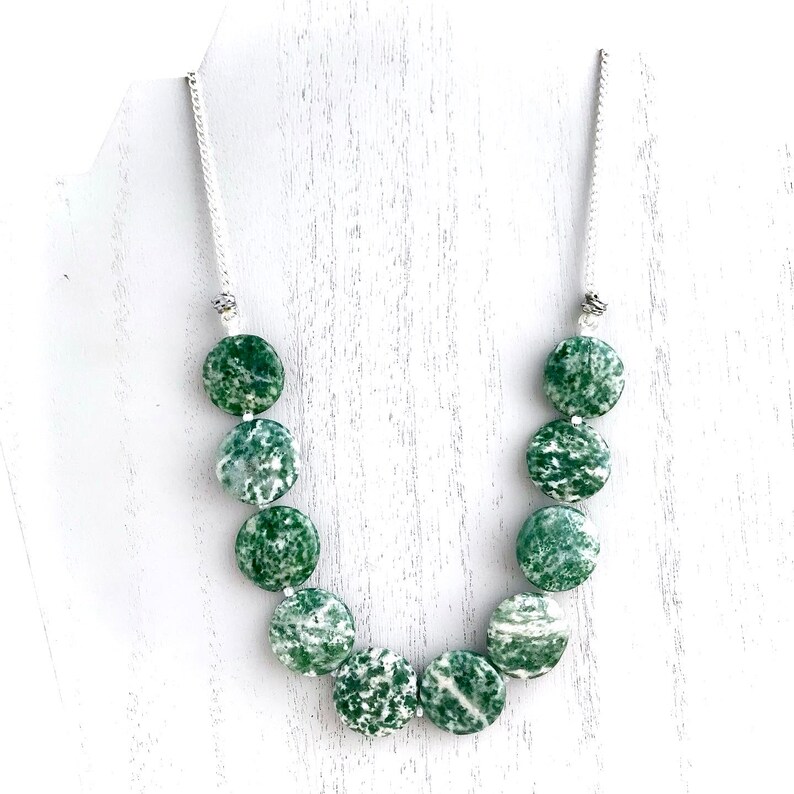 May include: A necklace featuring large, round, green and white speckled beads. The beads are strung on a silver-colored chain. The necklace is displayed against a white background.