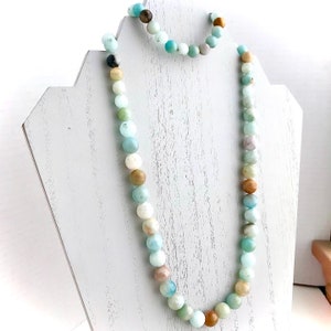May include: A light blue, green, and brown beaded necklace and bracelet set. The necklace is long and the bracelet is shorter. The beads are round and have a natural, polished look.