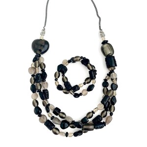 May include: A black and gray beaded necklace and bracelet set. The necklace is a triple strand of beads with a heart-shaped pendant. The bracelet is a single strand of beads.