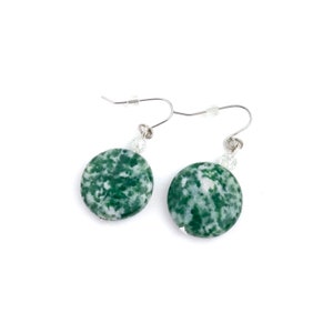 May include: A pair of dangle earrings featuring round, green and white speckled stone pendants. The earrings have silver-colored hooks and small clear beads. The stones have a natural, organic appearance, and the earrings are set against a white background.