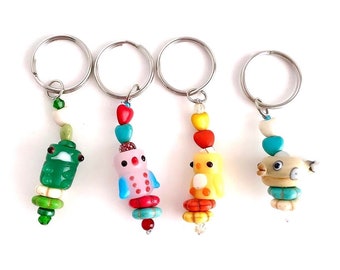 May include: Four colorful beaded keychains with different animal charms. The charms include a green frog, a pink bird, a yellow chick, and a gray fish. Each keychain has a silver key ring.