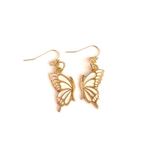 Peut inclure: Une paire de boucles d'oreilles en forme de papillon dorées avec des accents en émail blanc. Les boucles d'oreilles ont un design délicat et féminin.