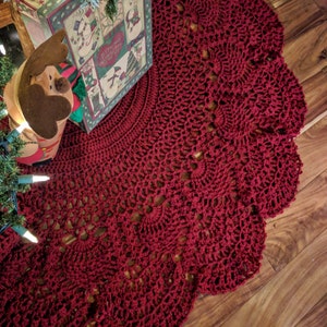 Puede incluir: Una falda de árbol de Navidad de crochet rojo con un borde festoneado. La falda está hecha con un delicado patrón de encaje.