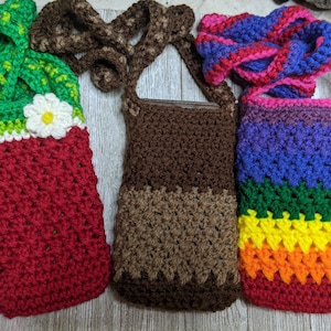 May include: Three crocheted phone cases with different color patterns. The first case is red with green and white accents. The second case is brown with a brown and white pattern. The third case is rainbow colored with purple, green, yellow, orange, and red.