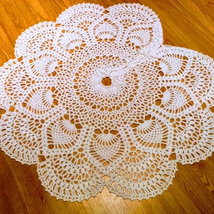 May include: White crocheted doily with a circular design and scalloped edges. The doily is made of delicate white thread and has a intricate pattern.