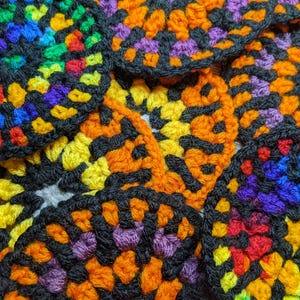 May include: A close-up of a pile of colourful crocheted coasters. The coasters are made with black, orange, yellow, purple, blue and green yarn. The coasters are circular and have a variety of patterns.