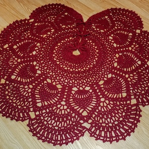 May include: A burgundy crocheted doily with a circular design. The doily is made of yarn and has a delicate, lacy pattern.