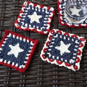 Puede incluir: Cuatro posavasos de ganchillo con un esquema de color rojo, blanco y azul. Cada posavasos presenta una estrella blanca sobre un fondo azul.