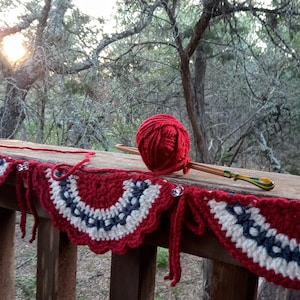 May include: A red, white, and blue crocheted garland with a ball of red yarn and a wooden knitting needle.