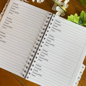 K&ouml;nnte beinhalten: Ein spiralgebundenes Notizbuch mit Seiten zum Aufzeichnen von Benutzernamen, E-Mails und Passw&ouml;rtern f&uuml;r Websites. Das Notizbuch hat Registerkarten, die mit Buchstaben des Alphabets beschriftet sind.
