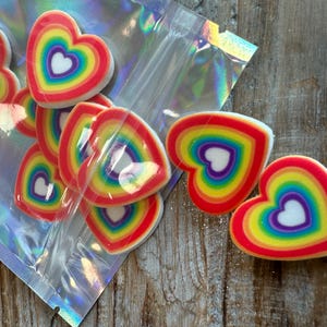 May include: A bag of rainbow heart-shaped resin charms. The charms are layered with red, orange, yellow, green, blue, indigo, and violet colors. The charms are in a clear plastic bag with a holographic finish.