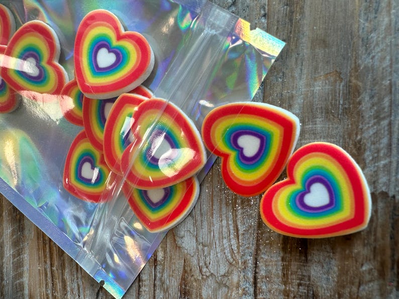 May include: A bag of rainbow heart-shaped resin charms. The charms are layered with red, orange, yellow, green, blue, indigo, and violet colors. The charms are in a clear plastic bag with a holographic finish.