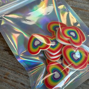 May include: A clear plastic bag filled with rainbow heart-shaped decorations. The hearts are made of a white material with a rainbow pattern.