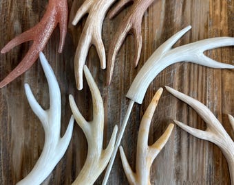 May include: A set of six decorative antlers in various shades of brown, white, and pink. The antlers are attached to wooden sticks, making them ideal for crafting or decorating.