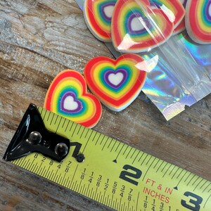 May include: A close-up of a measuring tape next to a bag of rainbow heart-shaped decorations. The tape measures 1 7/8 inches.