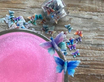 May include: A pink glass bowl with a sparkly surface, decorated with colorful butterfly sprinkles. The sprinkles are also in a small glass jar with a lid.