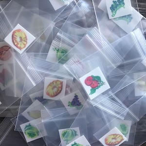Pode incluir: Uma pilha de sacos de pl&aacute;stico transparentes contendo pequenos adesivos coloridos com imagens de frutas, vegetais e outros alimentos.