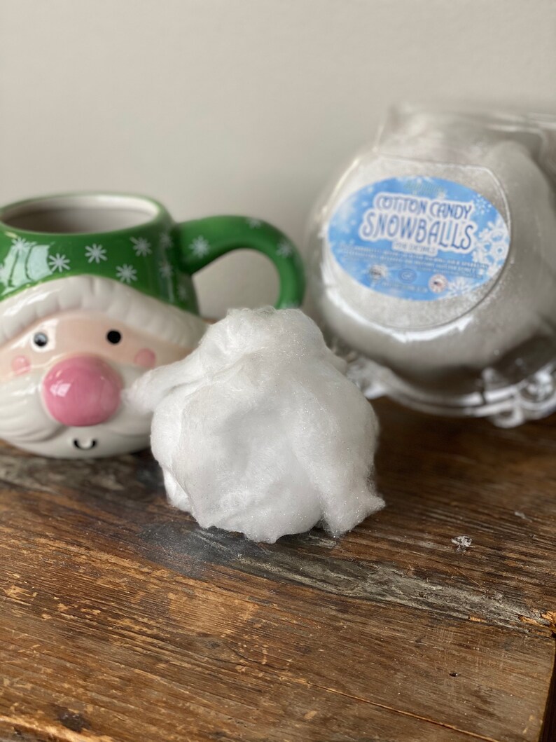 May include: A white cotton candy snowball in a clear plastic container with a label that reads "Cotton Candy Snowballs". A green and white Santa mug is in the background.