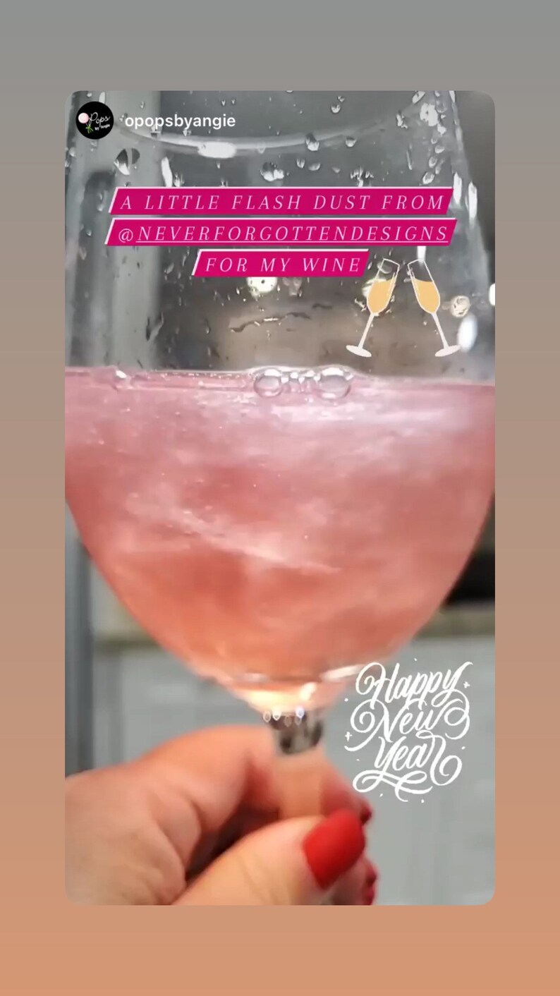 May include: A close-up of a wine glass filled with a pink, shimmering liquid. The text on the image reads "A LITTLE FLASH DUST FROM @NEVERFORGOTTENDESIGNS FOR MY WINE" and "Happy New Year".