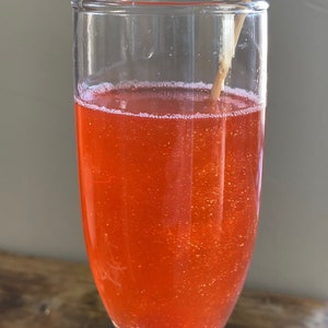 May include: A glass of orange sparkling drink with a wooden stirrer in it.