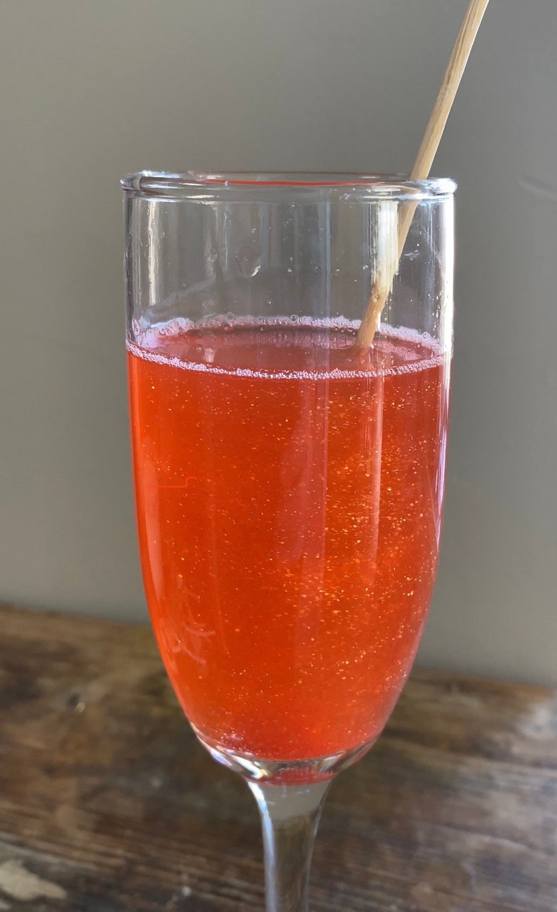 May include: A glass of orange sparkling drink with a wooden stirrer in it.