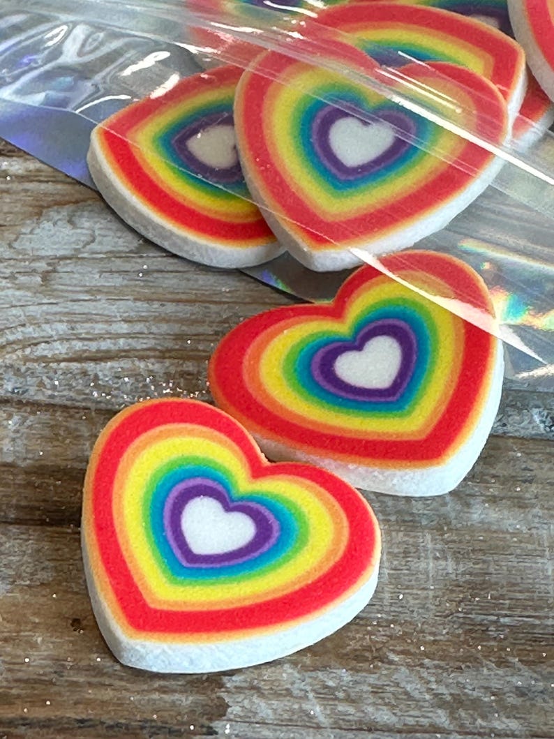 May include: A set of rainbow heart-shaped decorations. Each heart is made of a white material with a rainbow pattern and a white heart in the center.