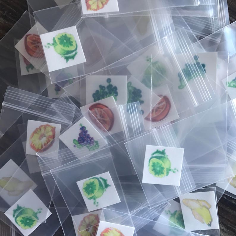 Pode incluir: Uma variedade de adesivos coloridos de frutas e vegetais em pequenos sacos de pl&aacute;stico transparentes. Os adesivos apresentam imagens de lim&otilde;es, limas, laranjas, uvas e outras frutas.