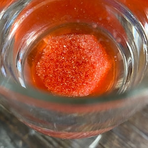 May include: A close-up of a glass container with a bright orange, granulated substance inside.