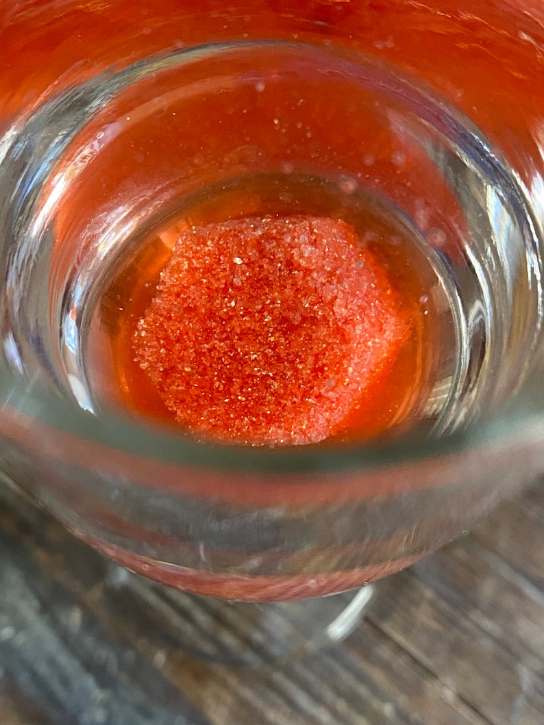 May include: A close-up of a glass container with a bright orange, granulated substance inside.