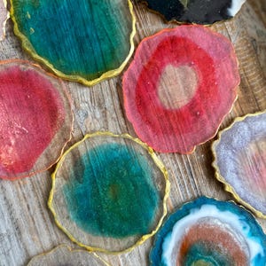 Puede incluir: Conjunto de posavasos de resina coloridos con bordes dorados. Los posavasos tienen un patrón único de tipo ágata con varios colores, incluyendo azul verdoso, rosa, morado y azul.