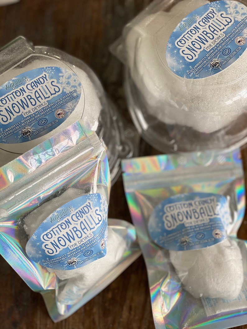 May include: Three clear plastic containers filled with white cotton candy snowballs. The containers have labels that say "Signature Cotton Candy Snowballs for Drinks".