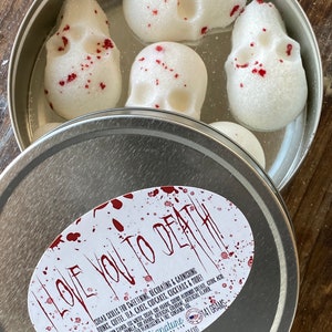 May include: A metal tin containing white sugar skulls with red accents. The tin lid features the text "I Love You to Death" and product information. The skulls are for sweetening and garnishing drinks, coffee, tea, cakes, and cocktails.