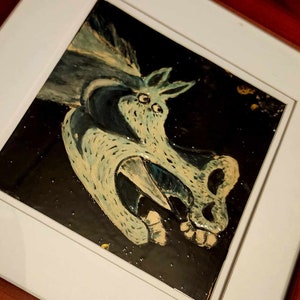Może przedstawiać: Namalowany obraz w ramie przedstawiający niebiesko-białą istotę z wielkimi ustami i ostrymi zębami. Istota znajduje się na czarnym tle z brokatem w kolorze złotym.