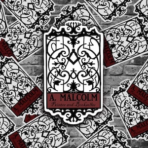 May include: A black and white sticker with an ornate design of a gate. The sticker has the text "A. Malcolm Printer and Bookseller" in a red banner.