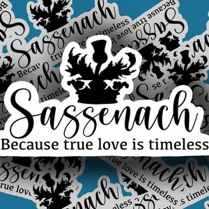 May include: A white sticker with black text and a black graphic of a stylized thistle. The text reads "Sassenach Because true love is timeless".