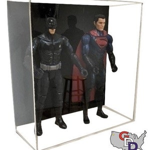 May include: A clear acrylic display case with a black background. Inside the case are two action figures, one of Batman and one of Superman. The figures are posed in a dynamic action stance. The case is perfect for displaying and protecting action figures.