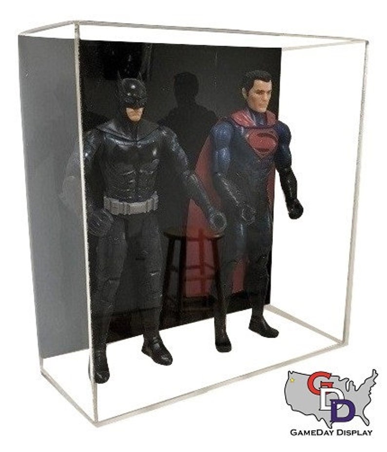 May include: A clear acrylic display case with a black background. Inside the case are two action figures, one of Batman and one of Superman. The figures are posed in a dynamic action stance. The case is perfect for displaying and protecting action figures.