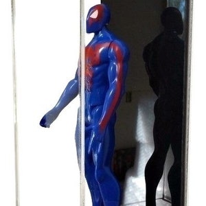 Puede incluir: Una vitrina de acr&iacute;lico transparente con un fondo negro. Dentro de la vitrina hay una figura de acci&oacute;n azul y roja de un superh&eacute;roe. La figura est&aacute; de pie sobre una base transparente.