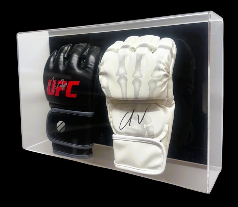 May include: A pair of black and white boxing gloves in a clear display case. The black glove has the UFC logo on it and the white glove is signed "DV".