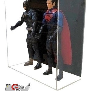 May include: Two action figures, Batman and Superman, are displayed in a clear acrylic display case. Batman is wearing a black suit and cape, while Superman is wearing a red and blue suit with a red cape. The figures are posed in a dynamic action stance.