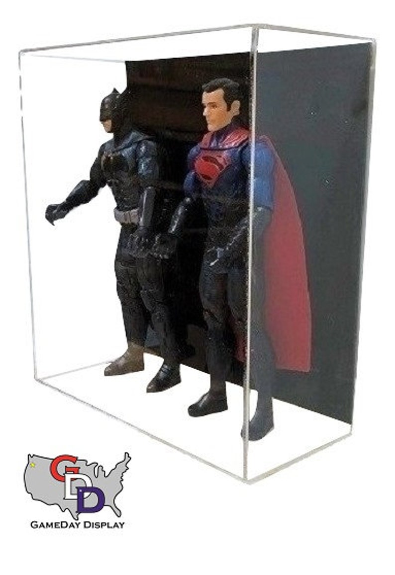 May include: Two action figures, Batman and Superman, are displayed in a clear acrylic display case. Batman is wearing a black suit and cape, while Superman is wearing a red and blue suit with a red cape. The figures are posed in a dynamic action stance.